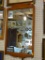 FRAMED WALL MIRROR; THIS IS A RECTANGULAR MIRROR WITH A WOODEN FRAME. THE TOP AND BOTTOM ARE
