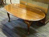 WOODEN COFFEE TABLE; OVAL TOPPED MAHOGANY COFFEE TABLE WITH SCALLOPED BOTTOM RAILS. THIS TABLE SITS