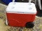 RED COLEMAN COOLER; RED AND WHITE COOLER MADE BY COLEMAN. THIS COOLER HAS A WHITE TOP WITH 4 CUP