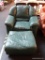GREEN LEATHER ARMCHAIR AND MATCHING OTTOMAN; CHAIR HAS ROUNDED STITCHED BACK WITH PADDED ARMS.