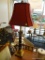 BRASS COLUMN STYLE LAMP; RED SQUARE SHAPED SHADE SITTING ON A BRASS AND BLACK COLUMN STYLE BODY WITH