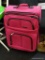 PINK LEISURE LUGGAGE CASE; HAS MULTIPLE FRONT FACING POCKETS AND BLACK HANDLES. HAS A BLACK