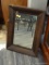 WOOD FRAMED WALL MIRROR; DARK STAINED WOOD FRAME AROUND MIRROR GLASS. ON THE BACK IS A STAMP THAT