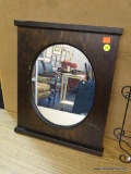 OVAL SHAPED MIRROR IN RECTANGULAR DARK WOODEN FRAME; HAS SMALL LEDGES AT TOP AND BOTTOM, MEASURES