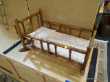 WOODEN ROCKING DOLL CRADLE; TURNED SPINDLED SIDES, PINK AND WHITE FLORAL PADDING AND PILLOW INSIDE.