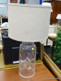 GLASS TABLE LAMP; THIS TABLE LAMP HAS A LINEN LIKE DRUM SHAPED SHADE AND SITS ON A CLEAR GLASS BASE