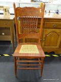 VINTAGE PRESSED BACK SIDE CHAIR; HAS A SHELL PATTERN CREST, SPINDLE STYLE BACK, AND A CANE BOTTOM