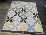 QUILT; IS BLACK, WHITE, PINK, AND BLUE IN COLOR AND HAS A PUZZLE LIKE PATTERN. GREAT FOR CHILLY