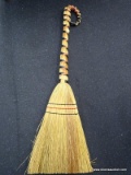 DECORATIVE STRAW BROOM; NATURAL COLORED HANDLE BOUND WITH RED AND BLACK STRANDS. TAPERED BROOM HEAD