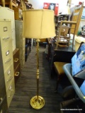 (R4) BRASS FLOOR LAMP; HAS A ROUND TAN SHADE WITH A HOOP FINIAL AND REEDED COLUMN BODY. MEASURES 14