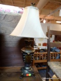 (R4) GOLD TONED LAMP; HAS AN ACANTHUS LEAF STYLE FINIAL WITH CREAM COLORED BELL SHADE, AN ACANTHUS