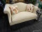 SINGLE CUSHION LOVE SEAT; SINGLE CUSHION CAMELBACK CREAM COLORED LOVE SEAT WITH MAHOGANY LEGS.