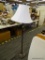 FLOOR LAMP; WHITE BELL SHAPED LAMPSHADE ATOP A POST WHICH IS DARK BRUSHED GREY METALLIC COLOR, WITH