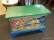DOGGIE TOY BIN; IS GREEN, BLUE, AND BROWN IN COLOR. HAS A LIFT LID THAT OPENS TO REVEAL STORAGE FOR