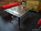 GLASS TOP COFFEE TABLE; RECTANGULAR BEVELED GLASS TOP SITTING ON A BLACK METAL BASE WITH WOVEN