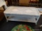 WHITE WICKER COFFEE TABLE; LATTICE APRON WITH LOWER STORAGE SHELF. MEASURES 42 IN X 21 IN X 16 IN.