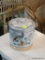 LIDDED JAR WITH WOVEN HANDLE; MADE IN JAPAN AND HAS A HAND PAINTED BIRD OF PARADISE ON THE FRONT