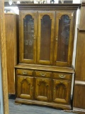 CHINA CABINET; DARK WOOD LIGHTED CHINA CABINET. UPPER PORTION OF CABINET CONTAINS A MOCK, GLASS