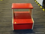 RED AND MAPLE STEP STOOL; HAS LIFT LID ON THE LOWER STEP THAT OPENS TO REVEAL STORAGE AND MEASURES