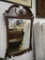 ORNATE WALL MIRROR; FEATURES A DARK WOOD, BEVELED FRAME WITH ORNATE SCROLL CARVINGS AND A DRAMATIC,