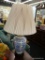 BLUE AND WHITE PORCELAIN LAMP; HAS A FLORAL PATTERN WITH BLACK PAINTED BASE, HAS SHADE AND FINIAL.