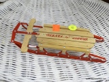 RADIO FLYER MODEL SLED; SMALL WOODEN MODEL SLED ON RED METAL FRAME. MEASURES 8.5 IN X 4 IN.