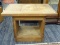 WOODEN SIDE TABLE; FEATURES A RECTANGULAR TOP AND TWO OPEN SIDES CONNECTED TO A RECTANGULAR BASE.