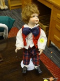 PORCELAIN MUSICAL DOLL; PORCELAIN DOLL DEPICTING A YOUNG BY WEARING A RED VEST, BLUE BOW TIE, PLAID