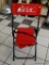 AFLAC FOLDING CHAIR; RED BACK AND SEAT ON BLACK FOLDING FAME. TOP HAS WHITE AFLAC LOGO, AND THE SEAT