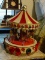 (BR2) TOY CAROUSEL; HOLIDAY THEMED CAROUSEL IN HUES OF RED AND WHITE WITH GREEN WREATH ACCENTS AND