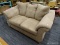 TAN LOVE SEAT; LARGE TWO-CUSHIONED LIVE SEAT, WING ARMS, ATTACHED PILLOWS, CURVED FEET.