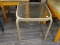 OUTDOOR PATIO SIDE TABLE; SQUARE GLASS TOP SITTING ON A TAN METAL BASE. MEASURES 1 FT 4 IN X 1 FT 4