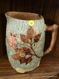 MAJOLICA PITCHER; HAS CHOCOLATE GLAZED AND WINE COLORED FLOWERS WITH A BRANCH STYLE HANDLE.