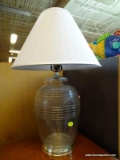 GLASS TABLE LAMP; WHITE PLEATED BELL SHAPED SHADE SITTING ON A LARGE GLASS BODY WITH ROUND METAL