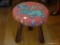 (LR) NEEDLE POINT STOOL; DRAGON NEEDLE POINT MOUNTED ONTO A WOODEN STOOL WITH 3 LEGS. MEASURES 11 IN