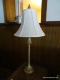 (DEN) BRASS TONE TABLE LAMP; WHITE BELL SHAPED SHADE SITTING ON A TALL CANDLESTICK STYLE BODY WITH