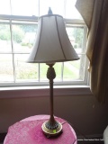 (FAM) BRASS TONE TABLE LAMP; WHITE BELL SHAPED SHADE SITTING ON A TALL CANDLESTICK STYLE BODY WITH