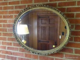 (SDRM) WALL MIRROR; OVAL WALL HANGING MIRROR IN A GOLD TONE FINISH ORNATE WOODEN FRAME. MEASURES 31