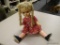 COLLECTIBLE DOLL; DOLL HAS BLONDE BRAIDED HAIR WITH A RED AND FLORAL PATTERN DRESS WITH BLACK SHOES.