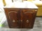 (R2) WOODEN END TABLE; DARK STAINED WOODEN END TABLE WITH 2 LOWER CABINET DOORS THAT HAVE A LOCKING