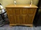 (R5) WOODEN CABINET; WOOD GRAIN CABINET WITH 2 BI-FOLD OPENING DOORS WITH METAL KNOBS THAT OPENS TO