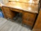 (R4) WOODEN DESK; WOOD GRAIN DESK WITH A MIDDLE DOVETAIL DRAWER THAT HAS METAL KNOBS ABOVE THE KNEE