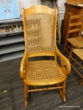 (R5) ROCKING CHAIR; WOODEN ROCKING CHAIR WITH SCROLL ARMS AND A WOVEN CANE BACK AND SEAT REST. IN