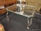 (R3) OCTAGONAL GLASS TABLE; THICK GLASS TABLE ON A METAL BASE. MEASURES 3 FT X 3 FT X 17.5 IN.