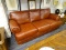 (R2) LEATHER SOFA; 3-CUSHION, RUST COLORED LEATHER, ROLL ARM SOFA WITH BUN FEET. IN GREAT CONDITION.