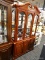 (R2) CHINA CABINET; 2 PC. WOODEN CHINA CABINET. TOP PIECE HAS A BROKEN ARCH PEDIMENT TOP AND 3 FRONT