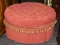 (R2) OTTOMAN; BUTTON TUFTED, ROUND OTTOMAN WITH A RED AND PINK FABRIC. HAS A SKIRT WITH TASSELS