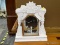 (R2) CLOCK BOX; WHITE PAINTED, ORNATE CARVED CLOCK BOX WITH FRONT DOOR. CLOCK HAS BEEN TAKEN OUT.