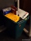 (R4) WASTE BUCK AND VHS TAPES; GREEN, SMALL TRASHCAN FULL OF ASSORTED VIDEO CASSETTE TAPES.