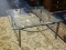 BEVELED EDGE, GLASS TOP, INDUSTRIAL STYLE COFFEE TABLE. MEASURES 38 IN X 38 IN. MISSING ONE OF THE